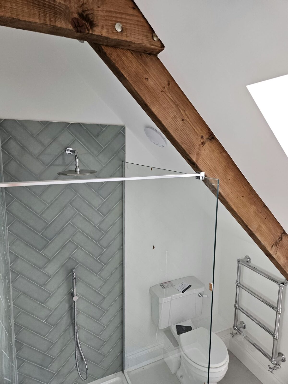 A green herringbone tiled shower beneath an exposed oak beam.